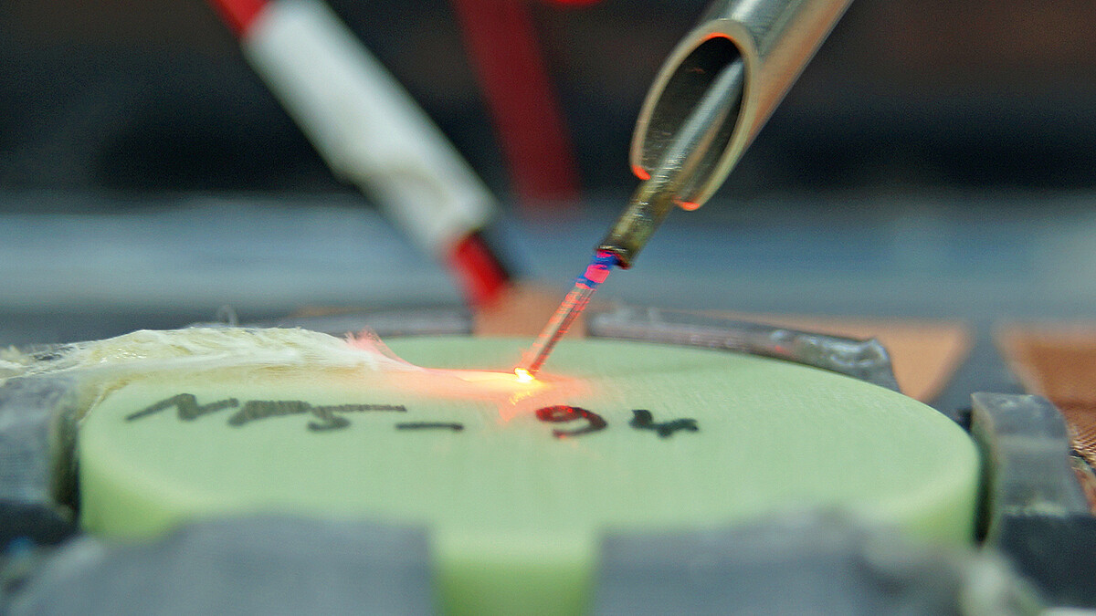 Aus einem Arbeitskanal tritt eine Laserfaser aus. Der Laserstrahl schmilzt Teile einer scheibenförmigen Probe auf. Dabei entsteht Schaum.