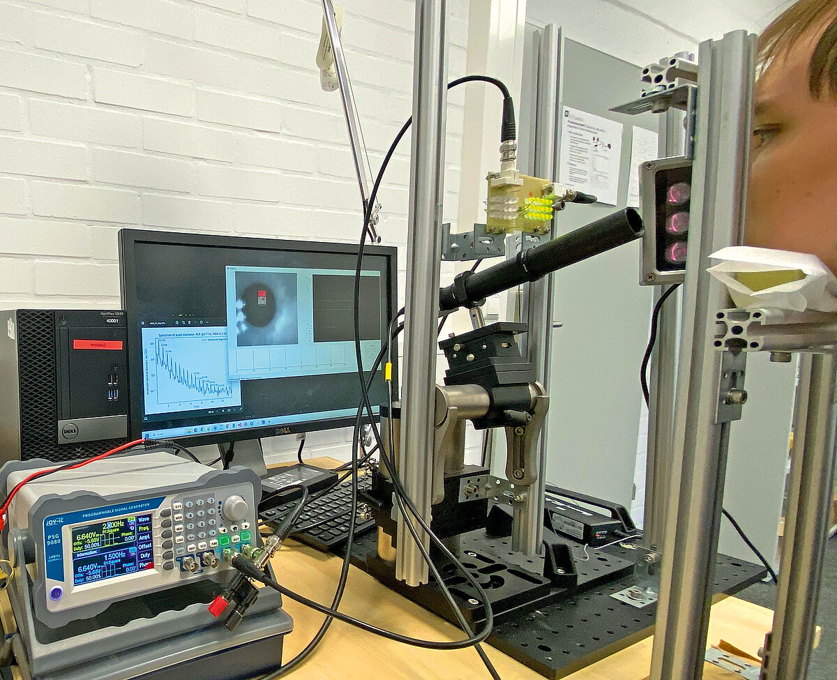 Eine Person stützt ihr Kinn auf eine Ablage. Eine teleskopartige Kamera ist auf das Auge gerichtet. Die Pupille erscheint auf einem Monitor. Weitere Messgeräte ergänzen den Aufbau.