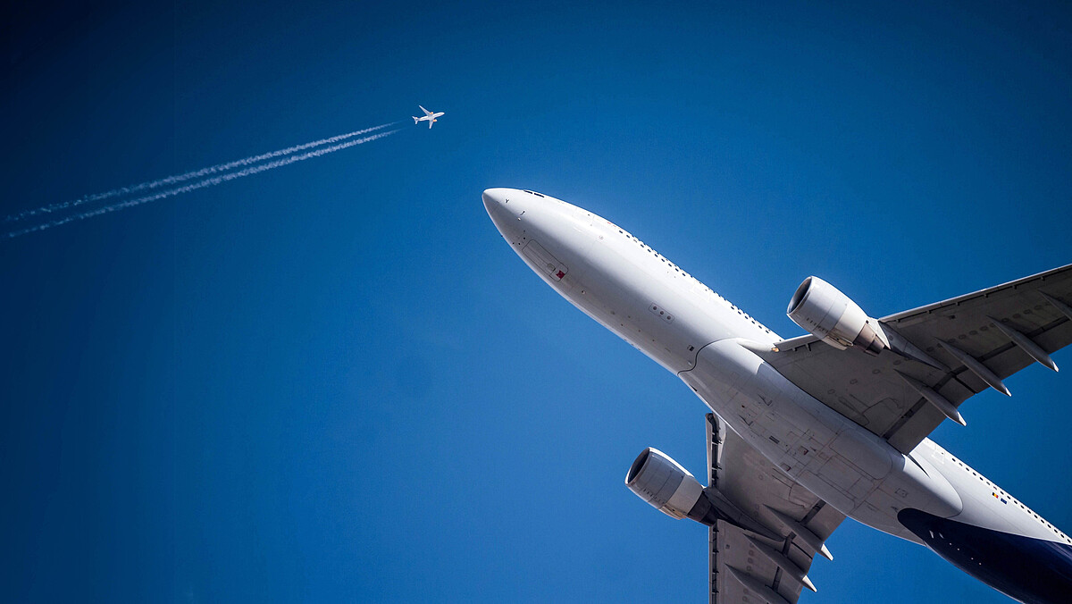 Das Bild zeigt zwei Flugzeuge am Himmel: eines aus der Nähe und ein weiter Entferntes mit zwei Kondensstreifen.