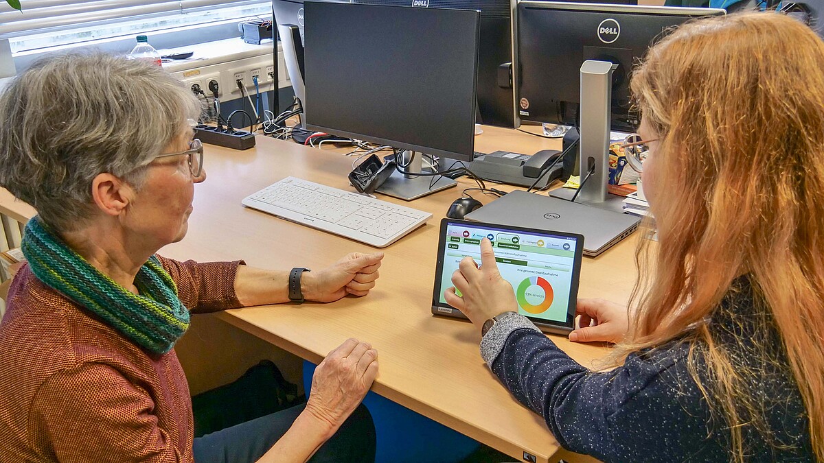 Eine junge Frau erklärt einer älteren Frau Funktionen an einem Tablet.